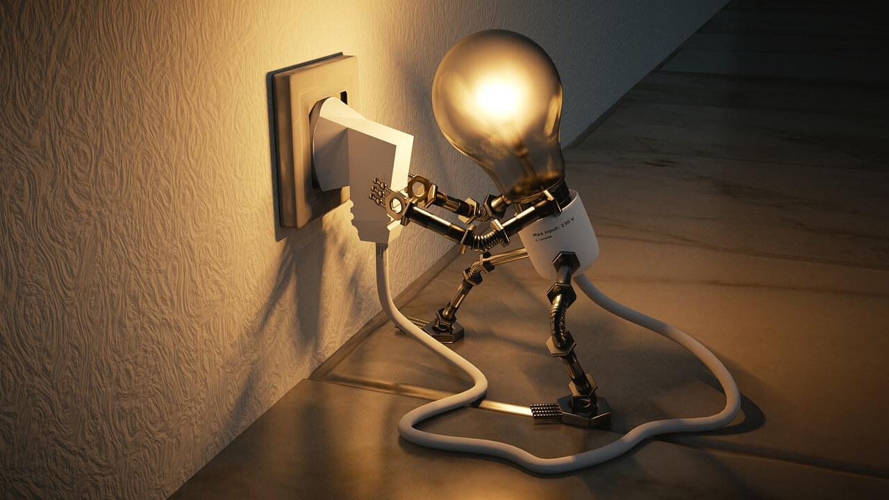 A light bulb with arms and legs plugging into an outlet, the light bulb is glowing, the background is a wall and a table